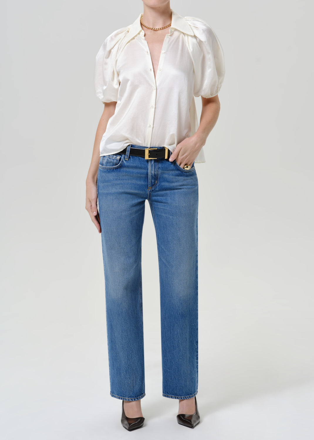Woman wearing a white puff sleeve button-up blouse with medium blue straight leg jeans on a grey background.