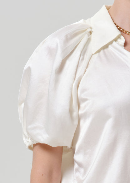 Close-up of a white puff sleeve button-up blouse on a grey background.