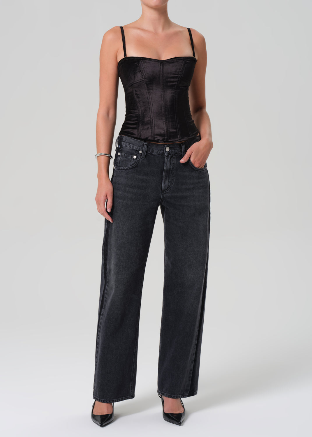 Person wearing a black corset and dark jeans on a plain background