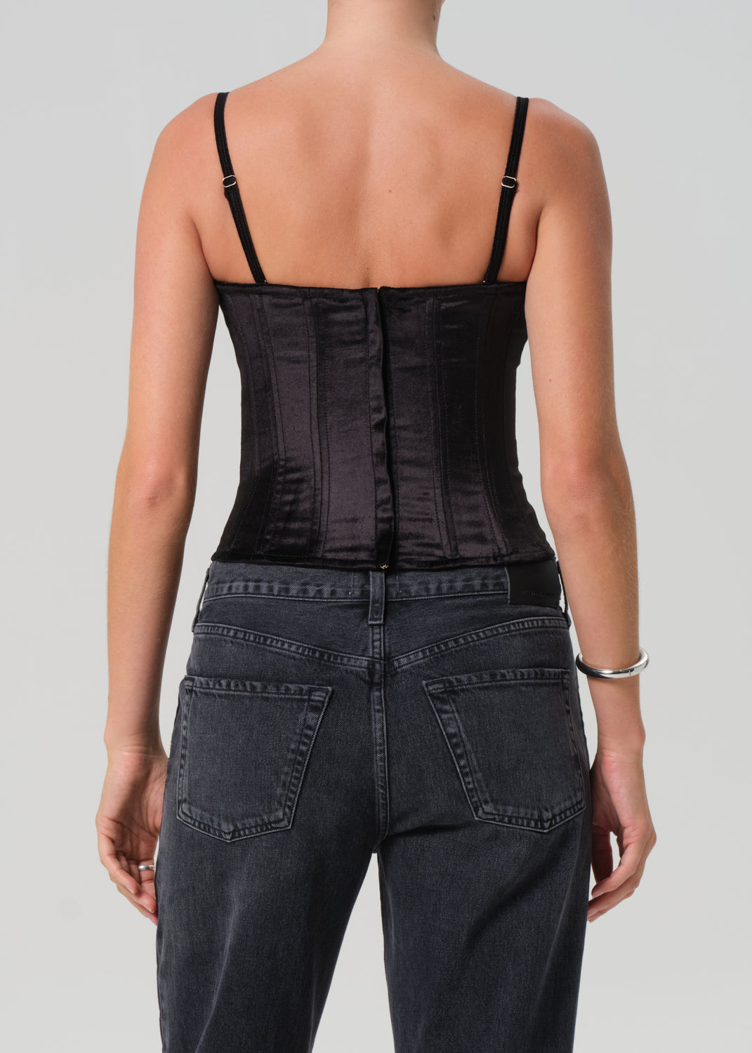 Person wearing a black corset and dark jeans on a plain background