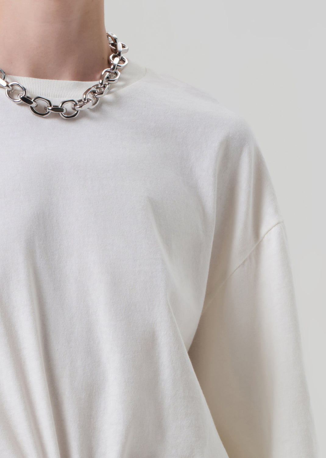Person wearing a silver chain necklace on a plain white background