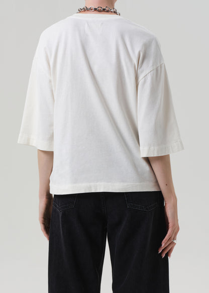 Person wearing a white oversized t-shirt and black pants on a plain background