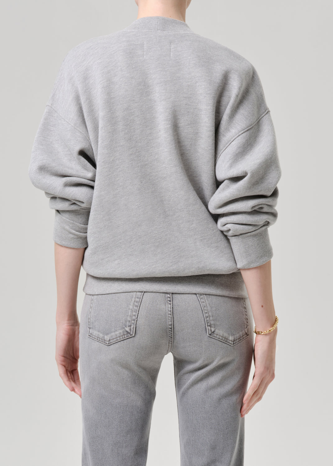 Person wearing a grey sweatshirt and jeans on a grey background