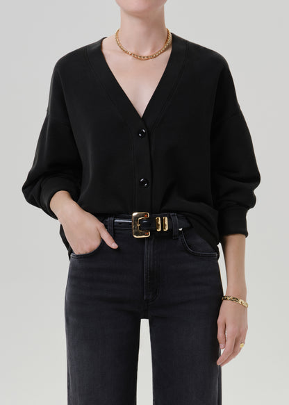 Person wearing a black V neck cardigan with dark wash jeans on a grey background