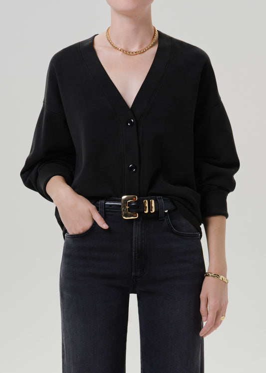 Person wearing a black V neck cardigan with dark wash jeans on a grey background