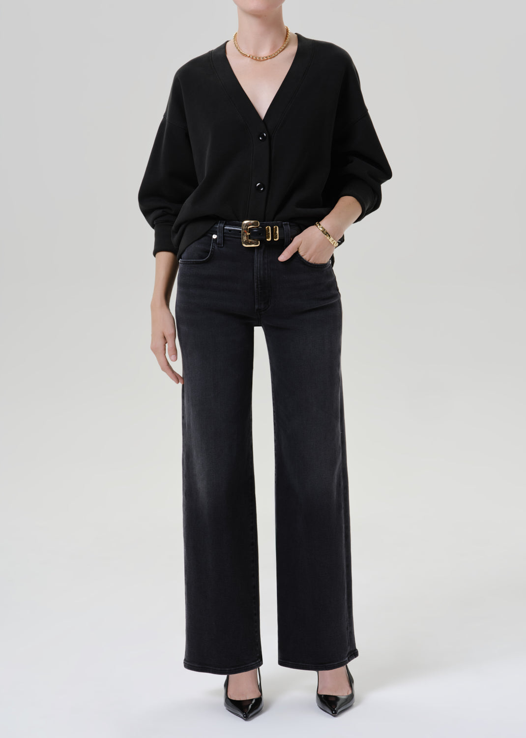 Person wearing a black V neck cardigan with dark wash wide leg jeans on a grey background
