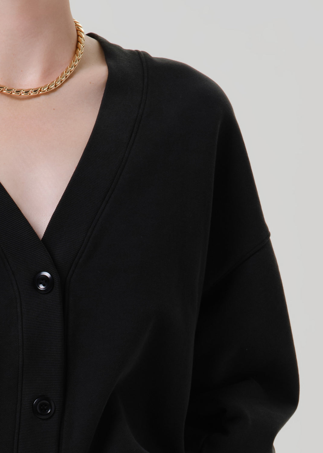 Person wearing a black V neck cardigan on a grey background