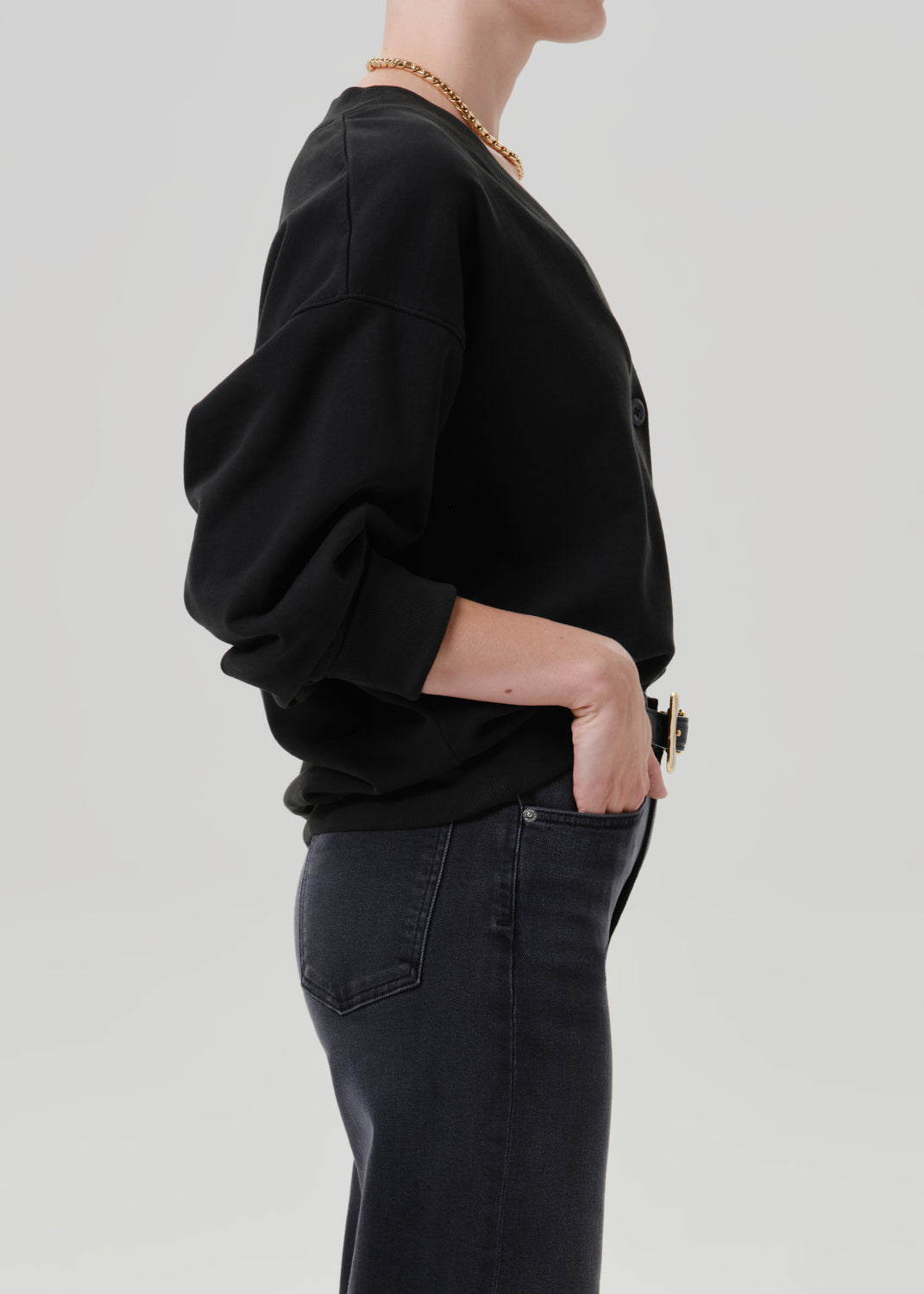 Person wearing a black V neck cardigan with dark wash jeans viewed from the side on a grey background