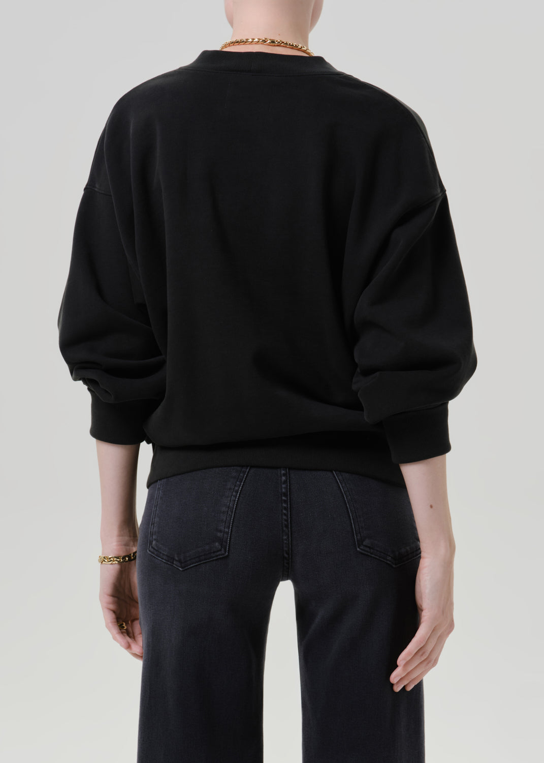 Person wearing a black V neck cardigan with dark wash jeans viewed from the back on a grey background