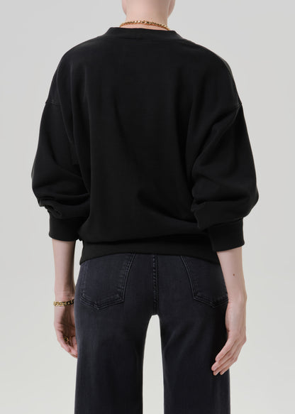 Person wearing a black V neck cardigan with dark wash jeans viewed from the back on a grey background
