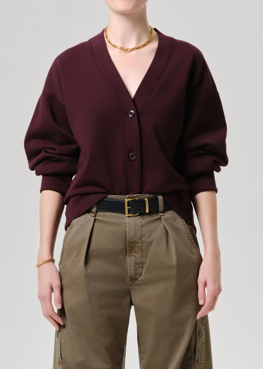 Person wearing a burgundy cardigan and beige pants on a grey background