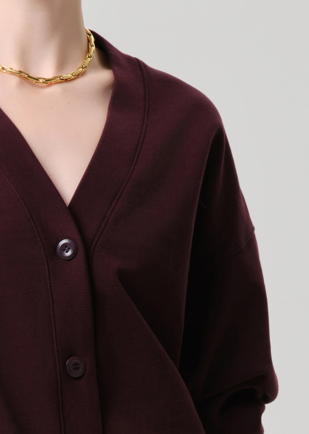 Close-up of a burgundy cardigan with a gold necklace on a grey background