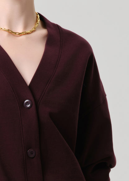 Close-up of a burgundy cardigan with a gold necklace on a grey background