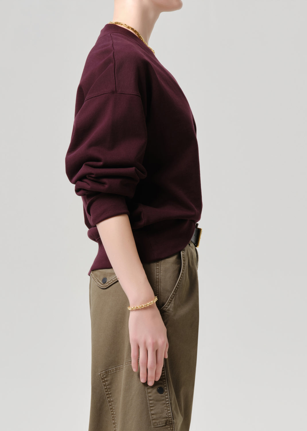 Person wearing a maroon sweatshirt and brown pants on a grey background