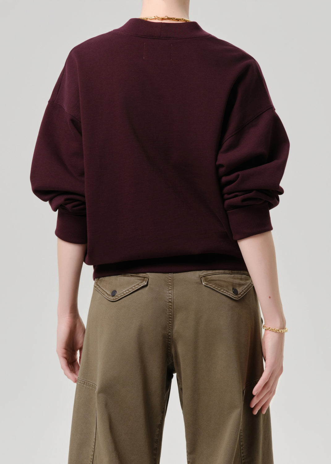 Person wearing a burgundy sweater and brown pants on a grey background