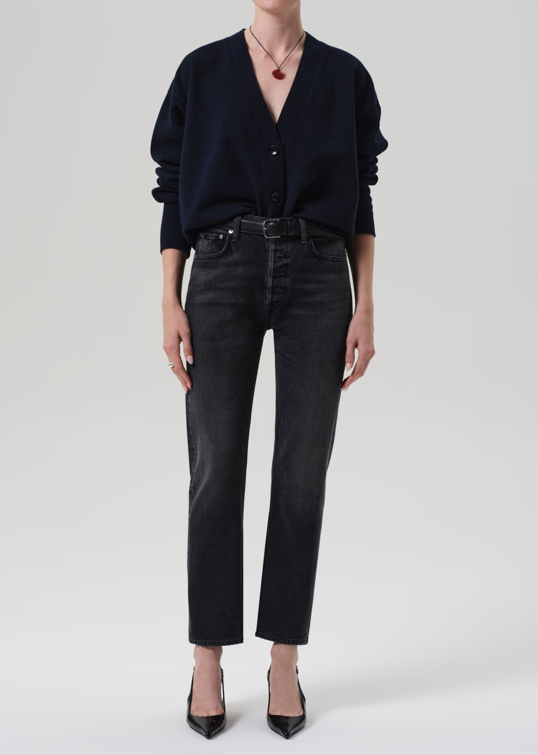 Person wearing a navy cardigan and dark jeans on a plain background