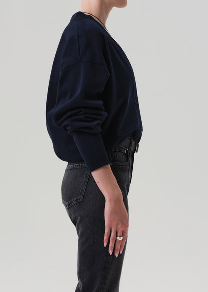 Person wearing a navy cardigan and dark jeans on a plain background