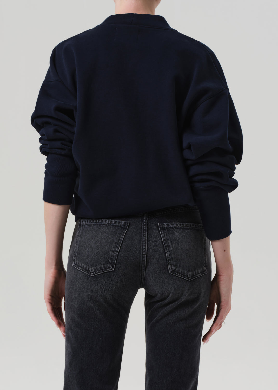 Person wearing a navy cardigan and dark jeans on a plain background