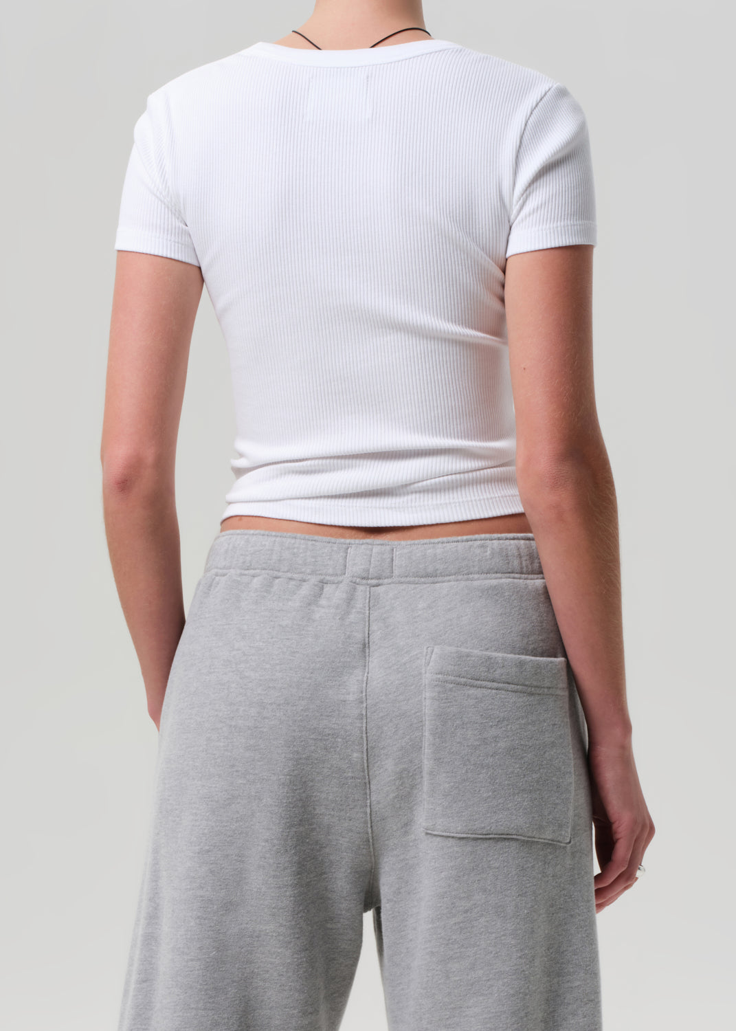Person wearing a white cropped t-shirt and gray sweatpants on a plain background