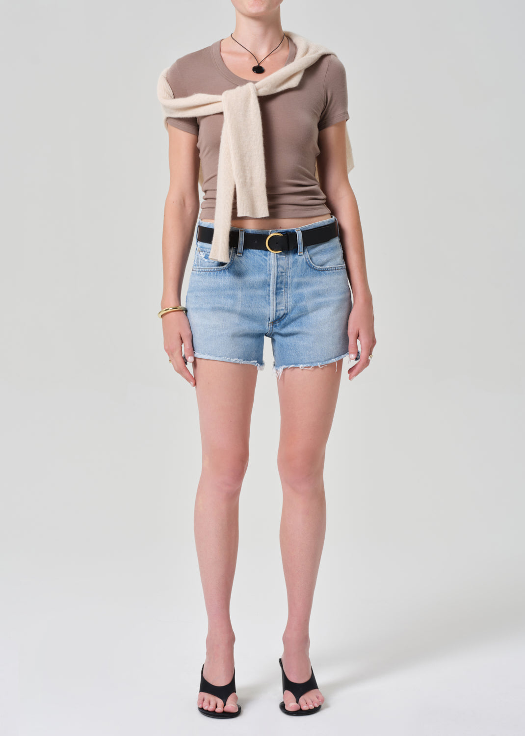 Person wearing a brown top, denim shorts, and a beige sweater on a plain background