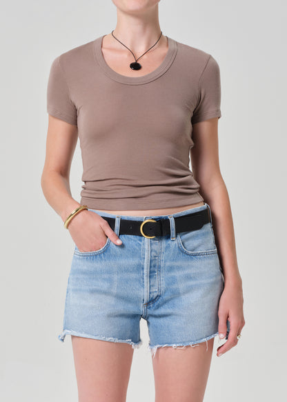 Person wearing a brown t-shirt and denim shorts on a plain background