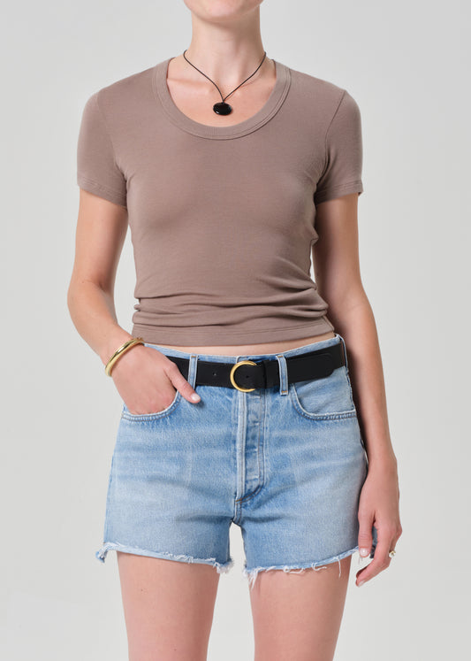 Person wearing a brown t-shirt and denim shorts on a plain background