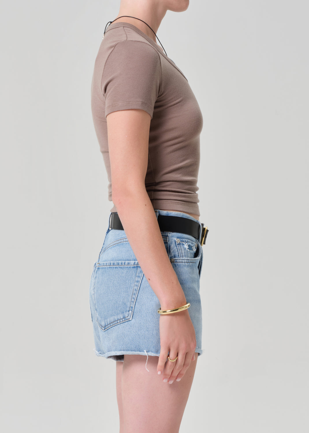 Person wearing a brown top and light blue denim short on a plain background