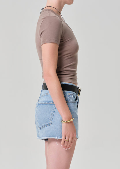 Person wearing a brown top and light blue denim short on a plain background