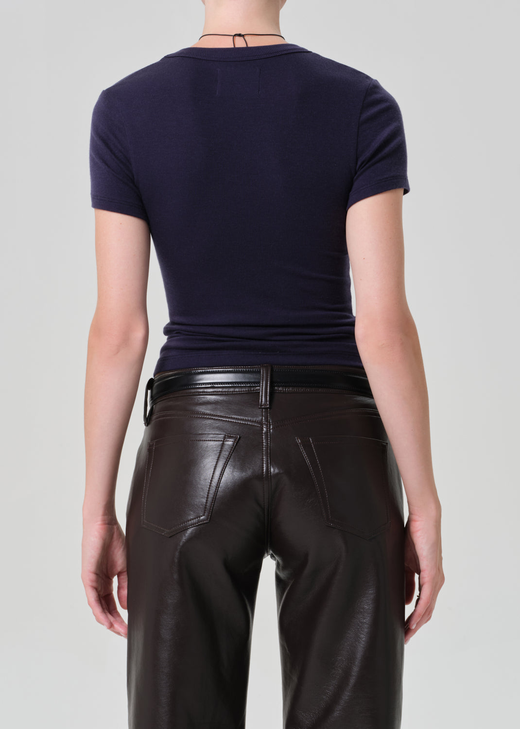 Person wearing a dark blue top and brown leather pants on a gray background