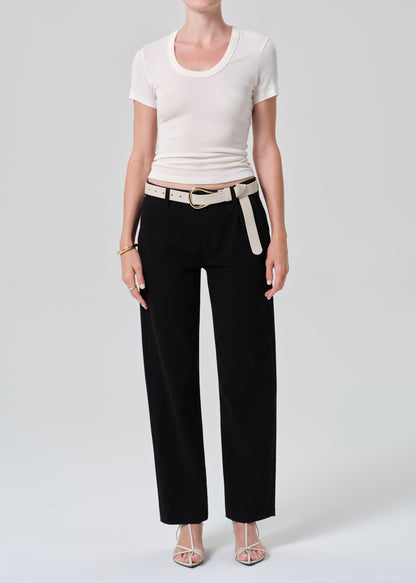 Person wearing a white crop top and black pants with a belt on a plain background
