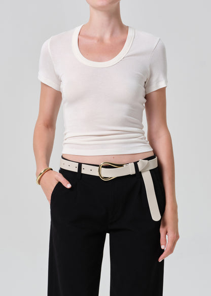 Person wearing a white crop top and black pants with a belt on a plain background
