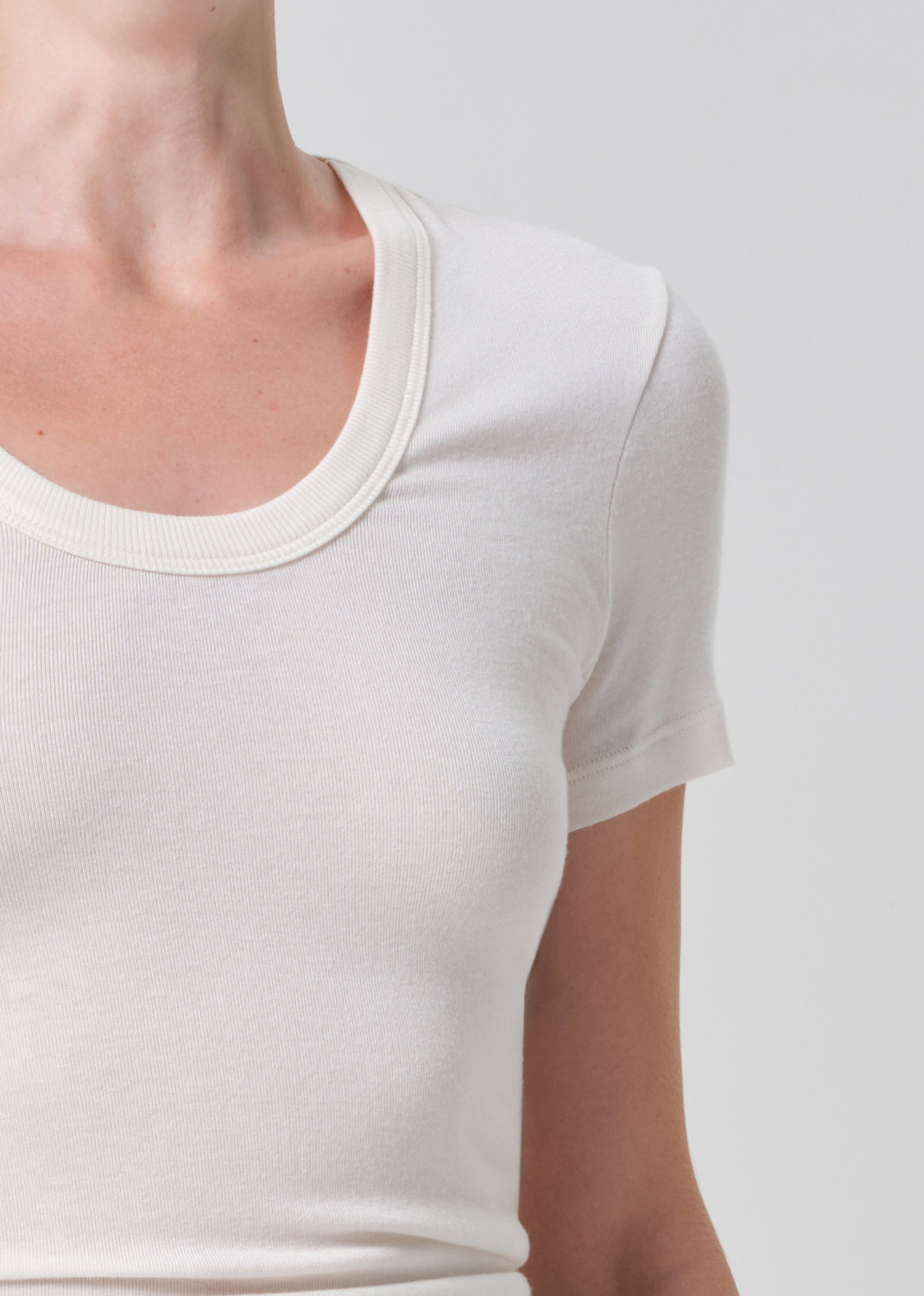 Person wearing a white crop top and black pants with a belt on a plain background