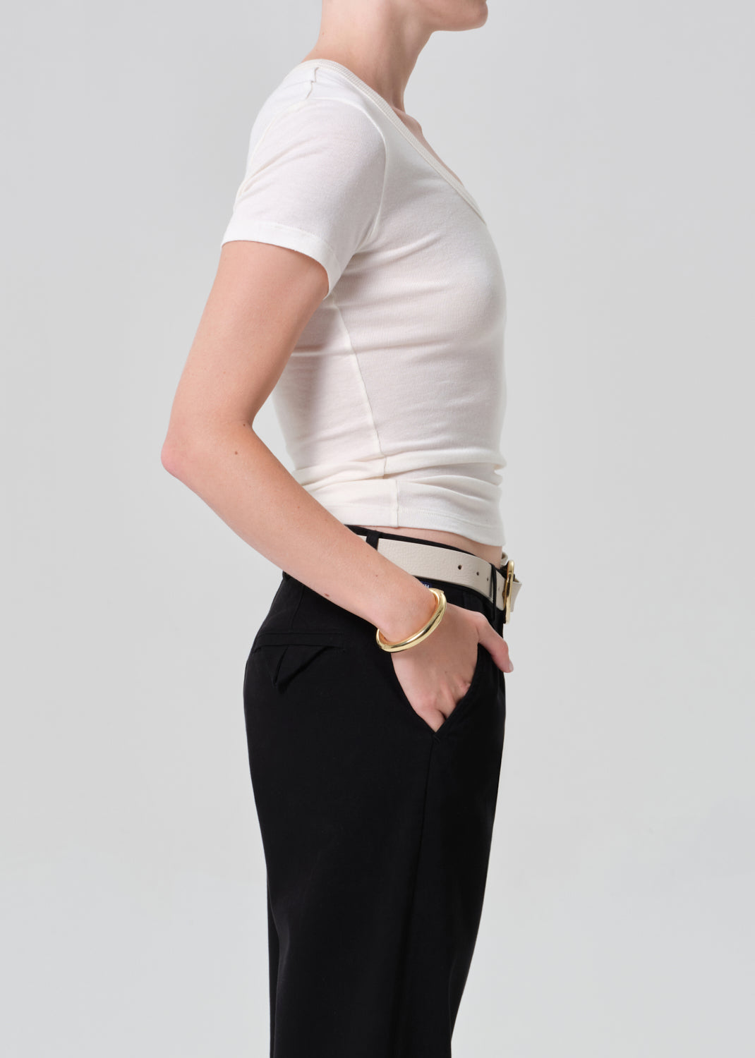 Person wearing a white crop top and black pants with a belt on a plain background