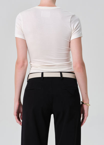 Person wearing a white crop top and black pants with a belt on a plain background