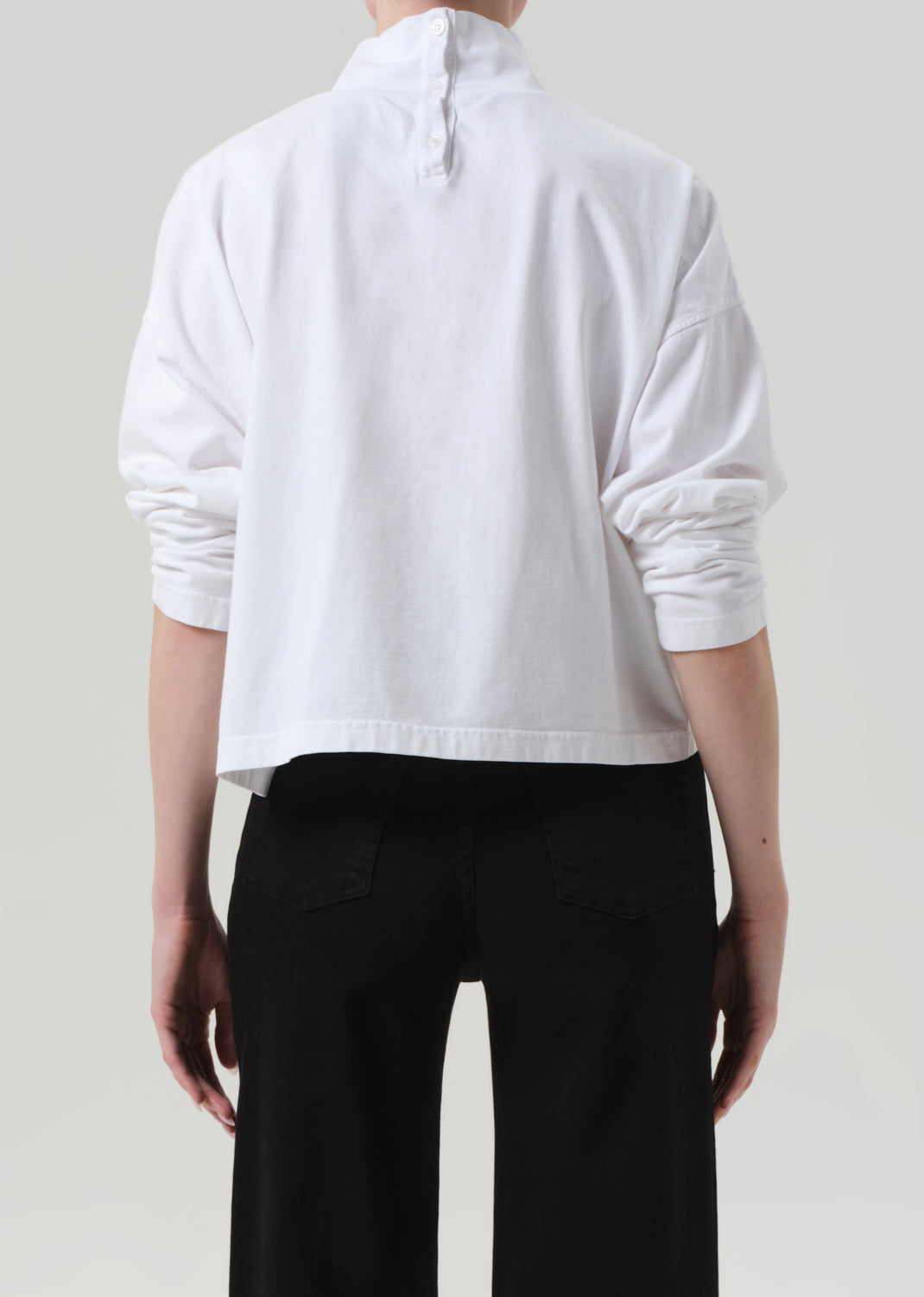 Person wearing a white long-sleeve shirt and black pants on a plain background