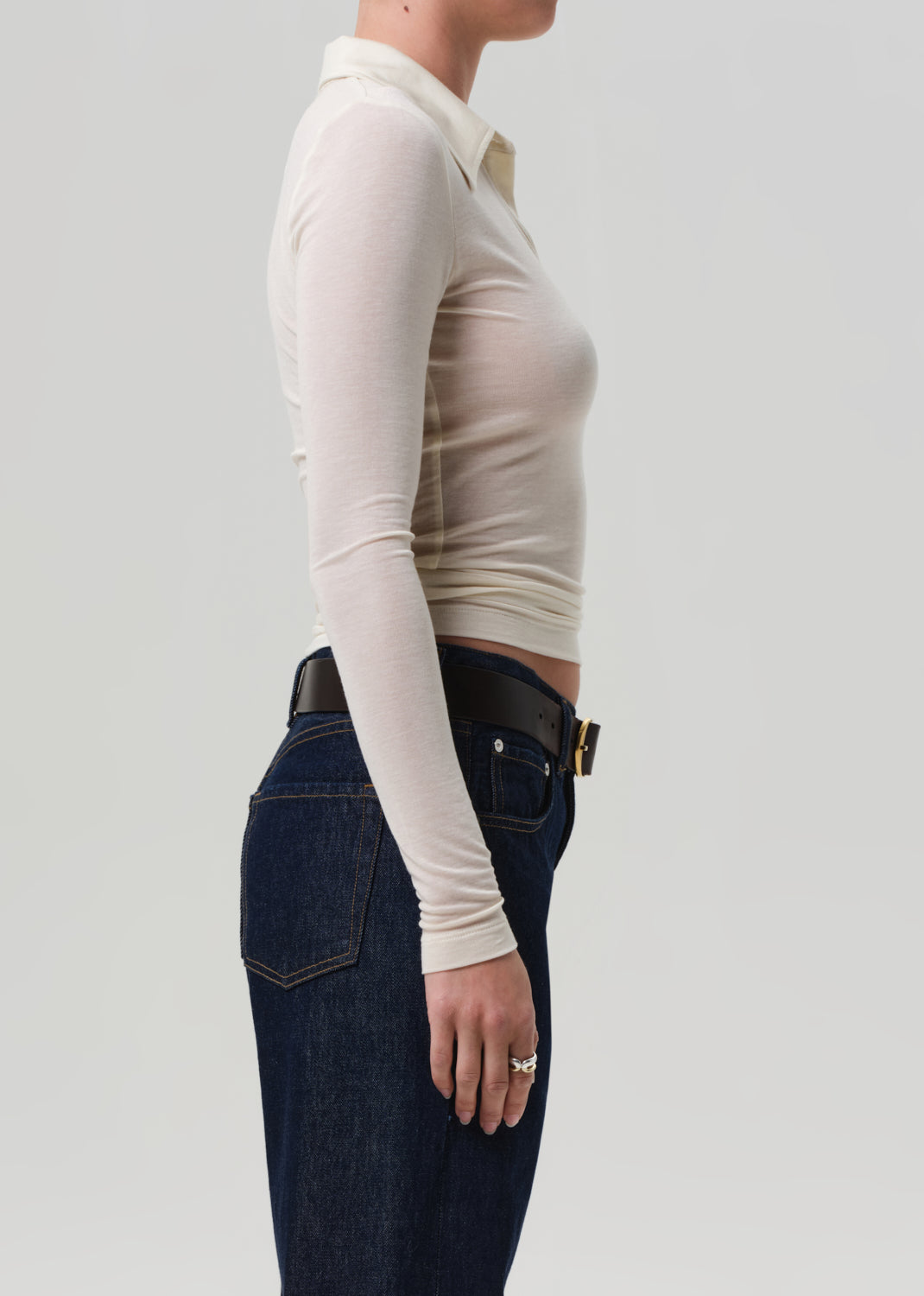 Person wearing a cream long-sleeve top and dark blue jeans on a light gray background