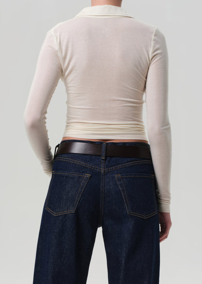 Person wearing a cream long-sleeve top and dark blue jeans on a light gray background