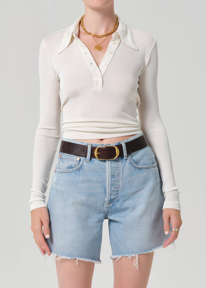 Person wearing a white long-sleeve shirt and denim shorts on a gray background