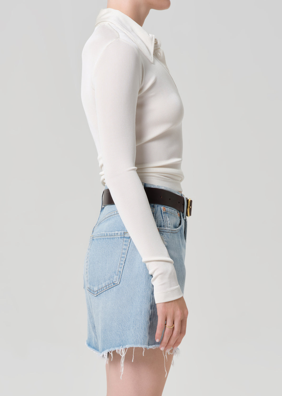 Person wearing a white long-sleeve top and light blue denim skirt on a plain background