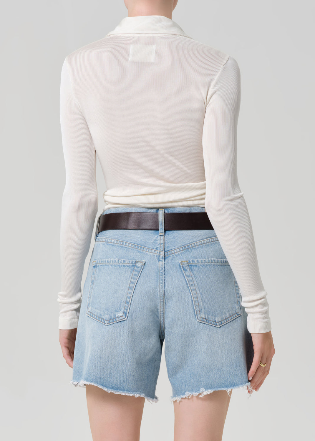 Person wearing a white long-sleeve shirt and light blue denim shorts on a gray background