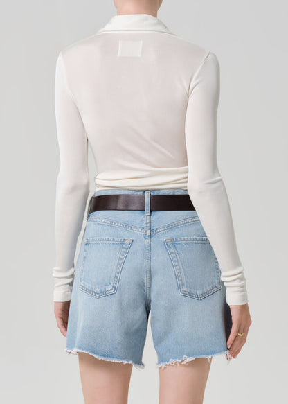 Person wearing a white long-sleeve shirt and light blue denim shorts on a gray background