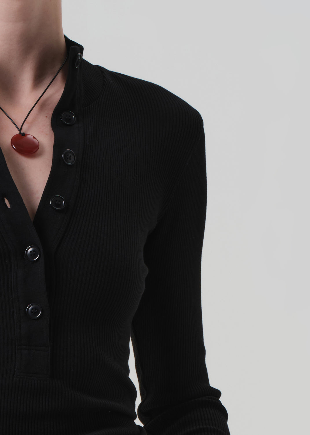 Black cardigan with a red pendant necklace on a plain background