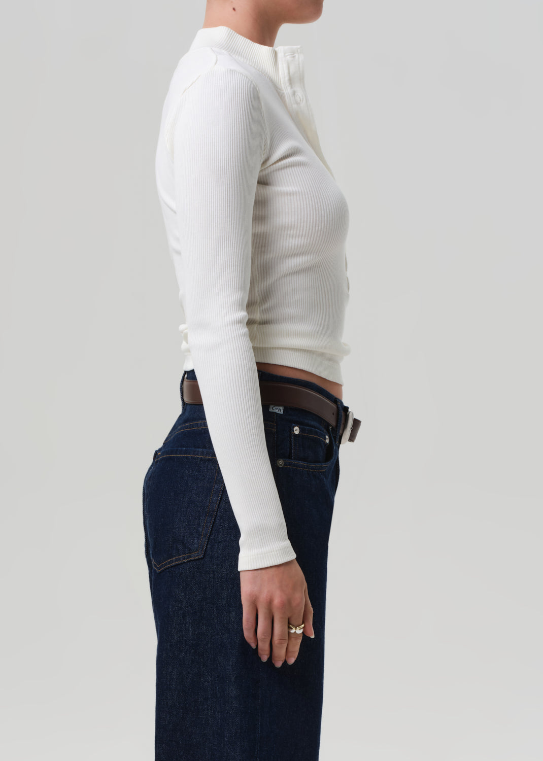 Person wearing a white long-sleeve top and dark jeans on a light gray background