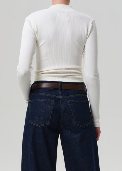 Person wearing a white long-sleeve shirt and dark blue jeans with a brown belt on a plain background