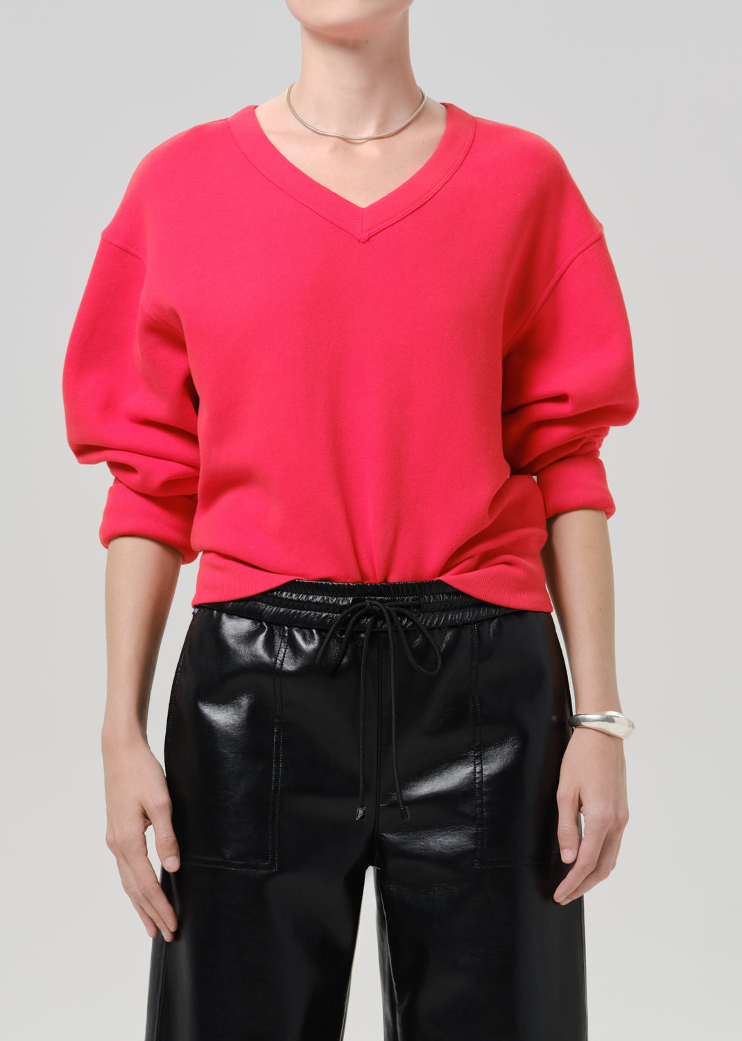 Person wearing a bright pink V neck sweater with black leather pants on a grey background