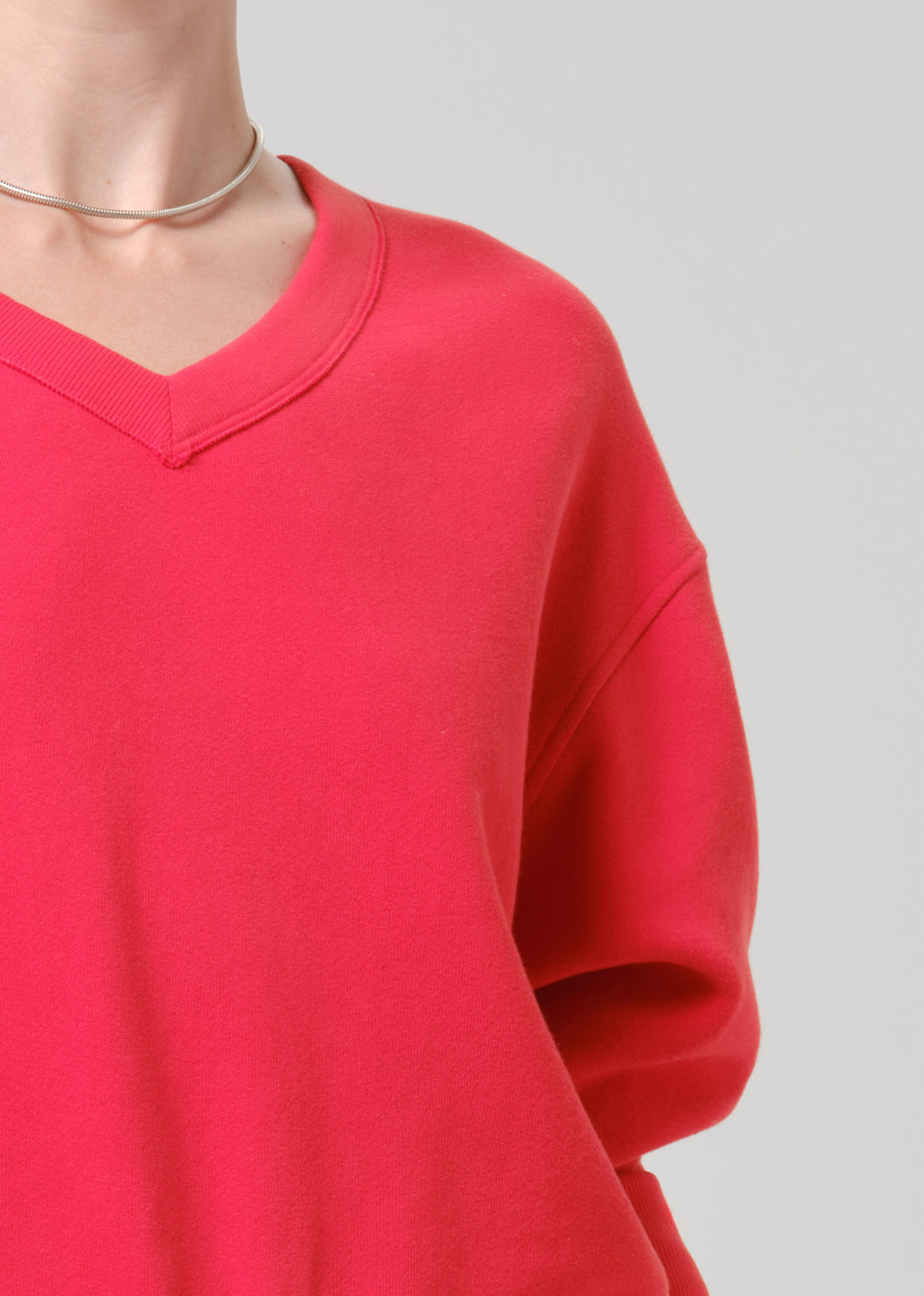 Person wearing a bright pink V neck sweater on a grey background