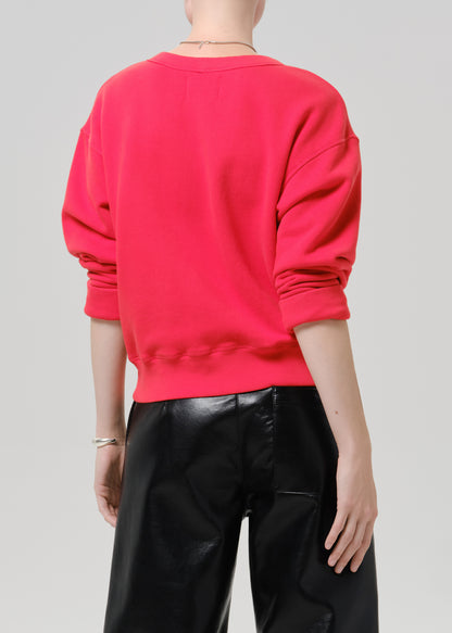 Person wearing a bright pink V neck sweater with black leather pants viewed from the back on a grey background