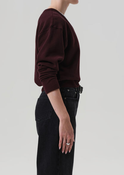 Person wearing a dark brown sweater and black jeans against a plain background