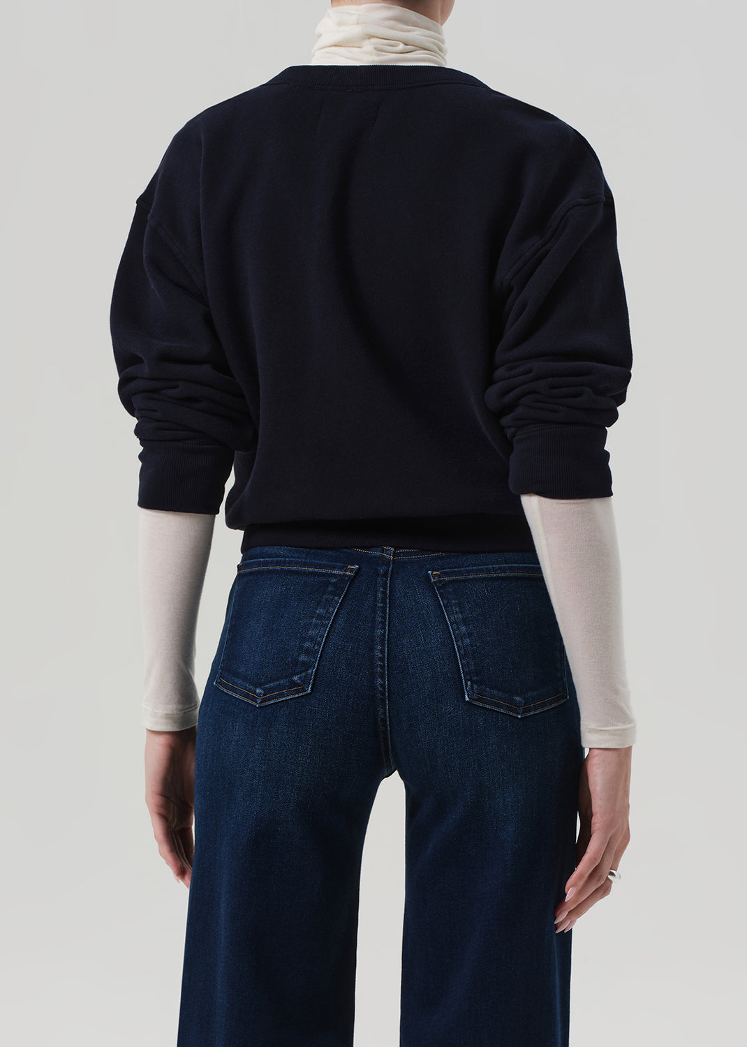 Person wearing a navy sweater and blue jeans on a plain background