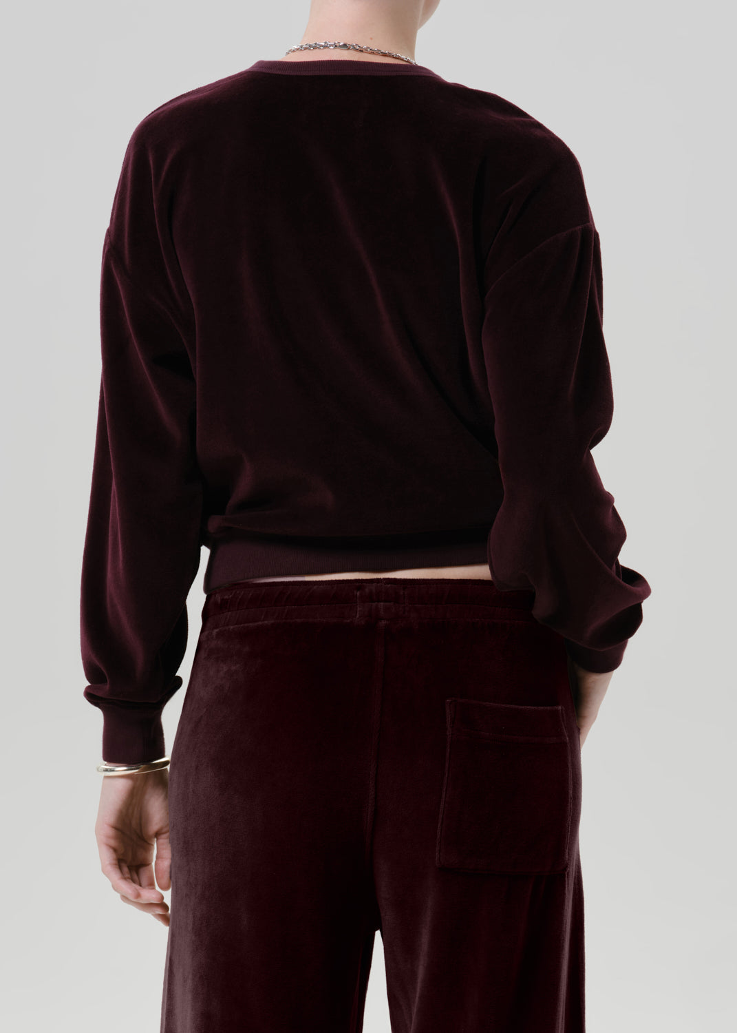 A person shown from the back wearing a dark burgundy velvet long-sleeve top and matching velvet pants against a grey background.